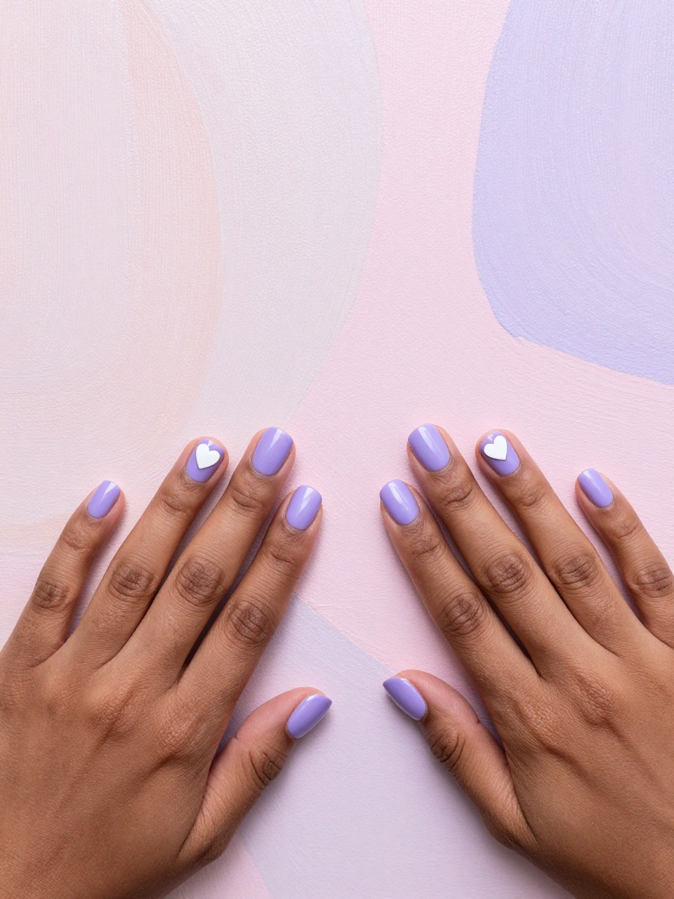 Top-down view of black feminine hands with short nails on a pastel abstract painting. Each nail is split into two soft purple tones. A tiny white heart sits at the color seam. The look is cheerful, soft, and coordinated.