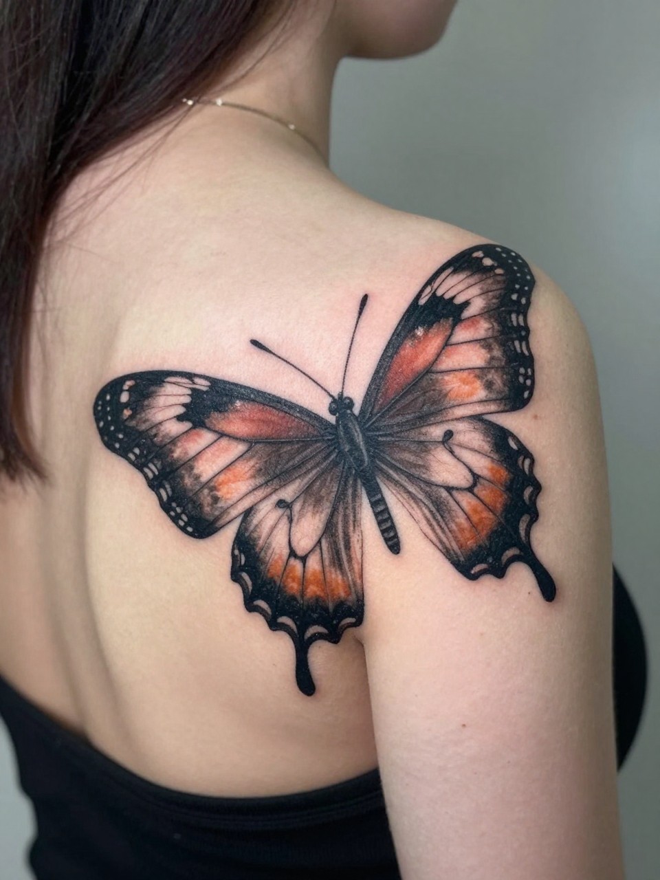 Over-the-shoulder view tattoo: a large, intricate butterfly tattoo on the back of the shoulder, its wings visible from both the back and side angles. Focus on the wingspan and detail."