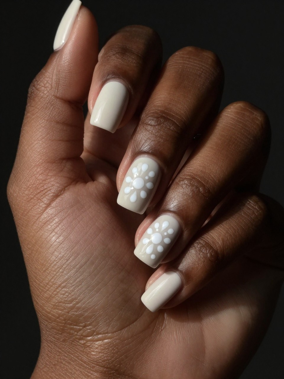 Side-angle shot of a black feminine hands under direct light. The nail is matte off-white. Glossy white micro-dots arranged in a flower shape are visible only when the light catches the shine. The look is sophisticated and secretive.