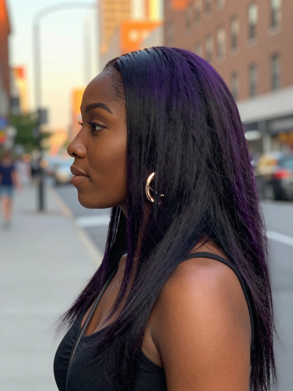 Photo of a black woman wearing long straight black hair with purple, side profile view, in a softly blurred city street background, golden hour glow, containing a small lived-in detail such as statement earrings peeking through and a crossbody strap on the shoulder, latest iPhone photo quality.