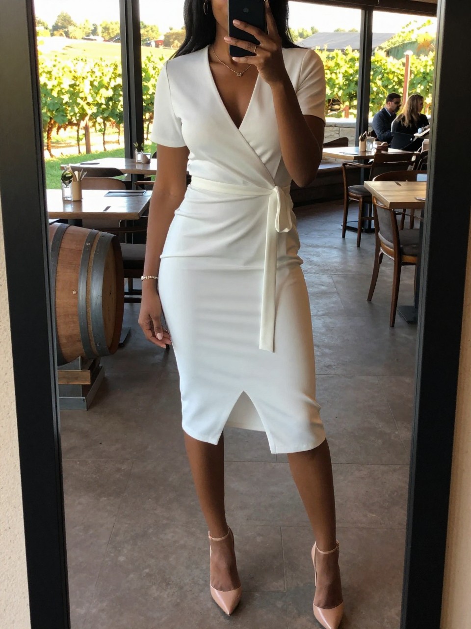 mirror selfie of a black woman in a white wrap dress and nude heels, standing at a winery or upscale restaurant, cropped at NECK so face doesn't show, at a winery, evening golden hour, iPhone photo quality.