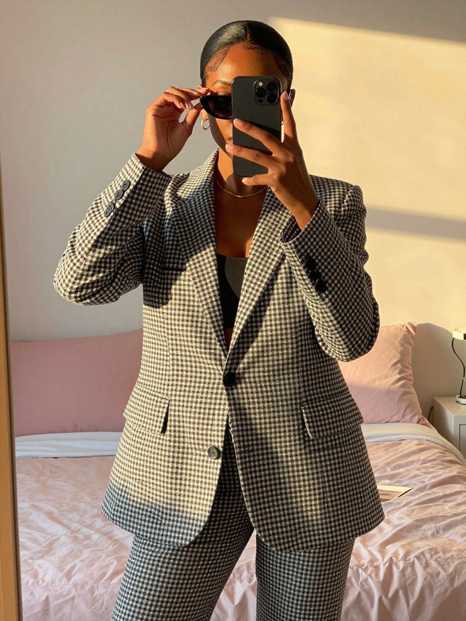 mirror selfie of a black woman in a gingham suit set, adjusting her sunglasses, cropped at NECK so face doesn't show, in a feminine-themed bedroom, evening golden hour, iPhone photo quality.