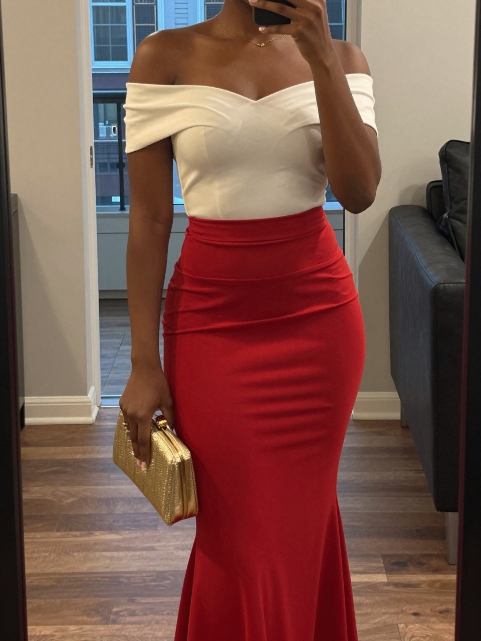 mirror selfie of a black woman in an off-the-shoulder top and a red mermaid skirt with a gold clutch, gently holding the clutch at her side, cropped at NECK so face doesn’t show, in a city apartment, warm moody lighting, iPhone photo quality.