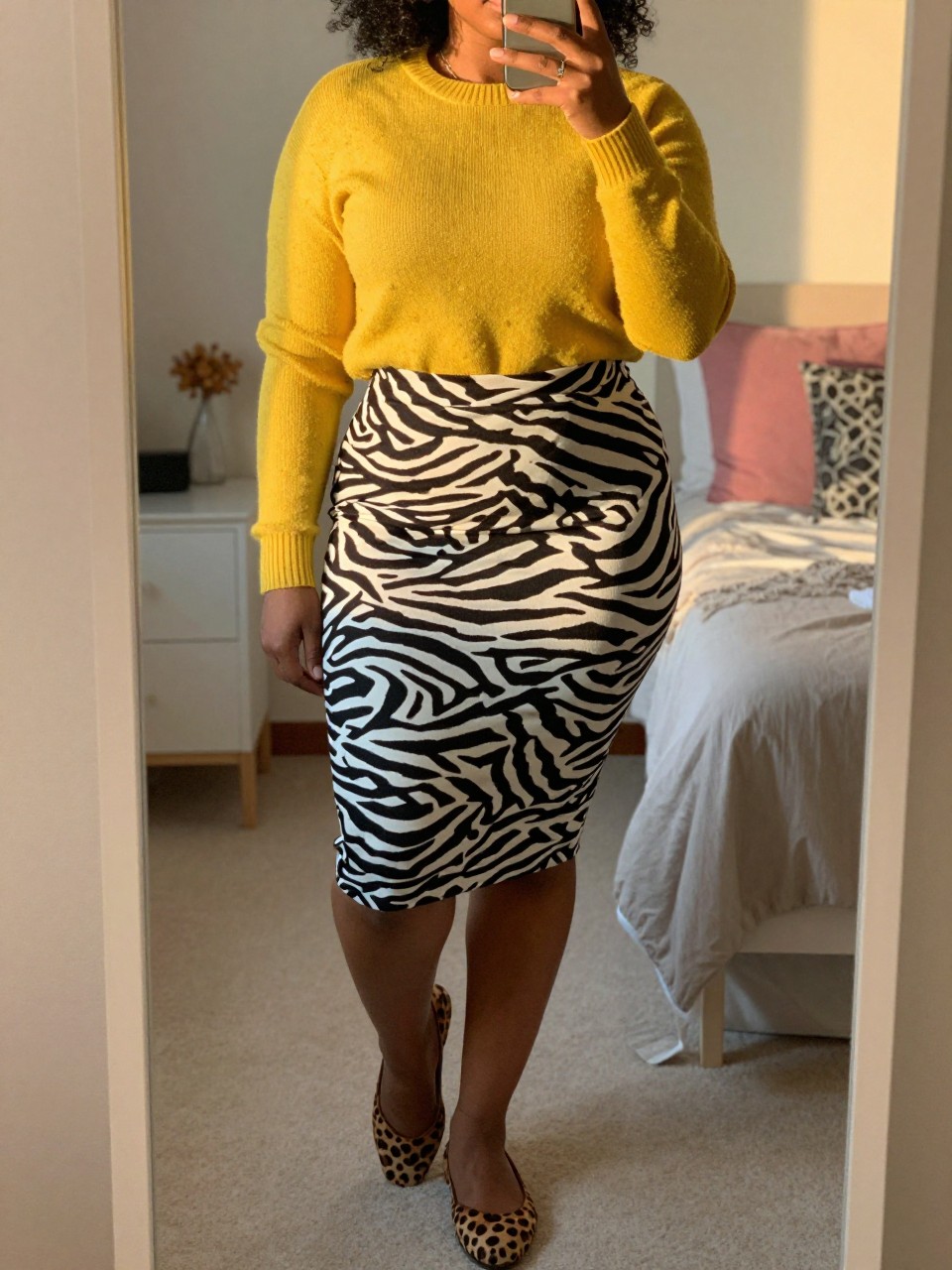 mirror selfie of a curvy black woman in a yellow sweater and a zebra print skirt with leopard print flats, standing with her weight on one leg, cropped at NECK so face doesn't show, in a feminine-themed bedroom, evening golden hour, iPhone photo quality.