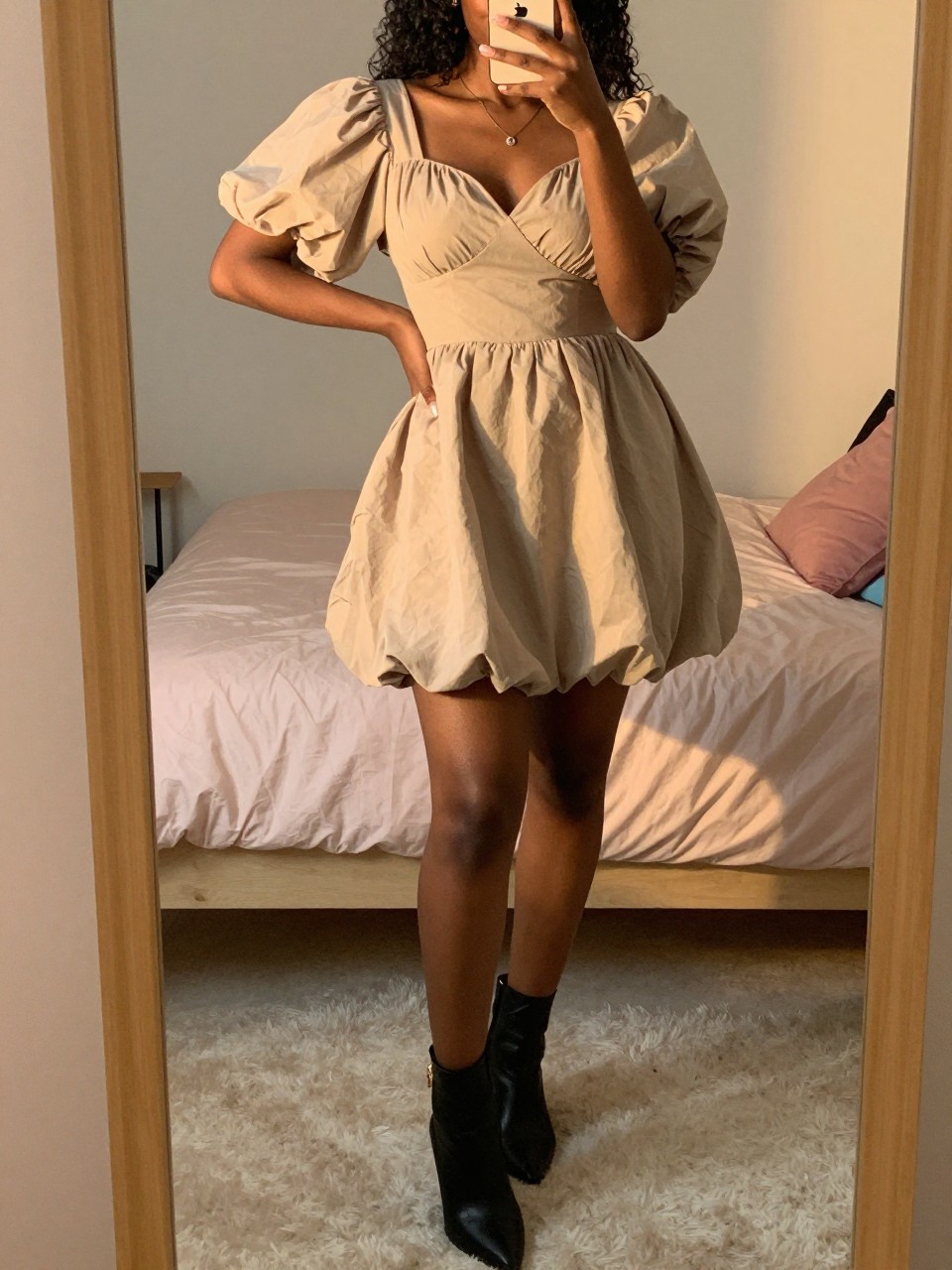 mirror selfie of a black woman in a puff-sleeve dress and ankle boots, posing playfully, cropped at NECK so face doesn't show, in a feminine-themed bedroom, evening golden hour, iPhone photo quality.