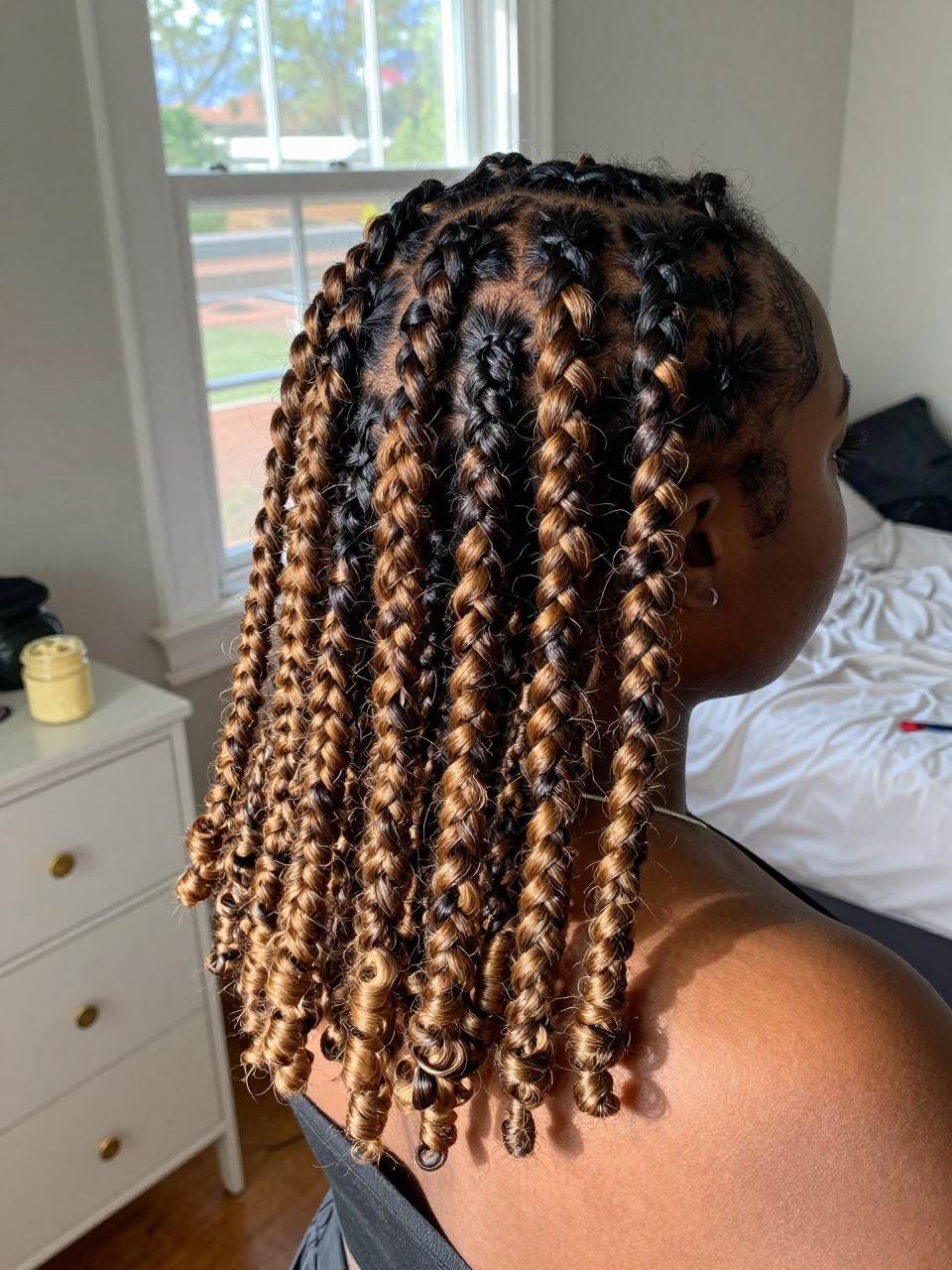 Photo of a Black woman wearing chunky natural twists with dark honey highlights placed through the front and lengths, back-of-head view to highlight details, in a sun-drenched bedroom, natural window light, containing a small lived-in detail such as gold cuffs on the dresser and a jar of twisting butter nearby, latest iPhone photo quality.
