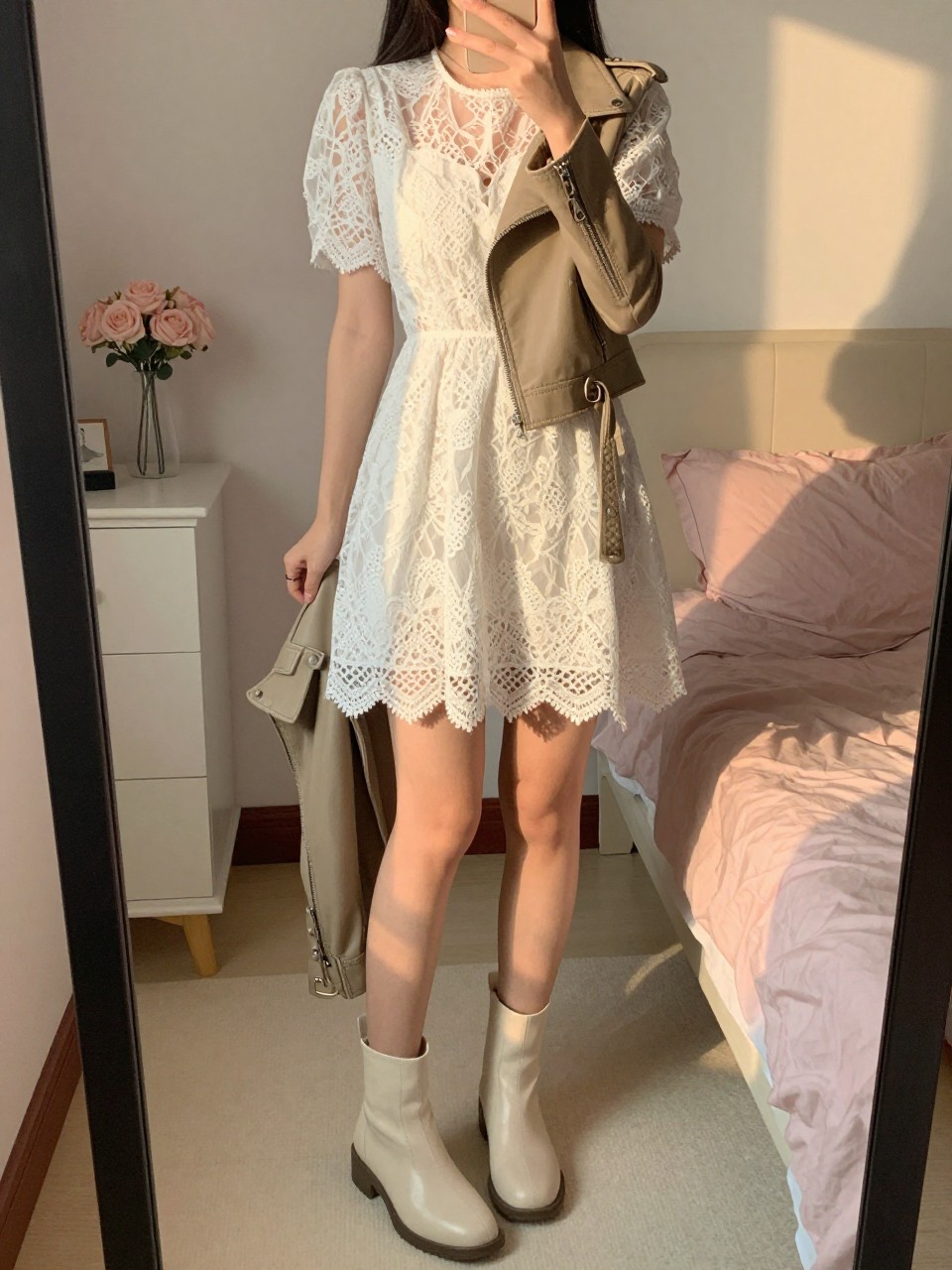 iPhone mirror selfie of a woman in a white lace dress and ankle boots, holding a moto jacket, cropped at NECK so face doesn't show, in a feminine-themed bedroom, evening golden hour, iPhone photo quality.