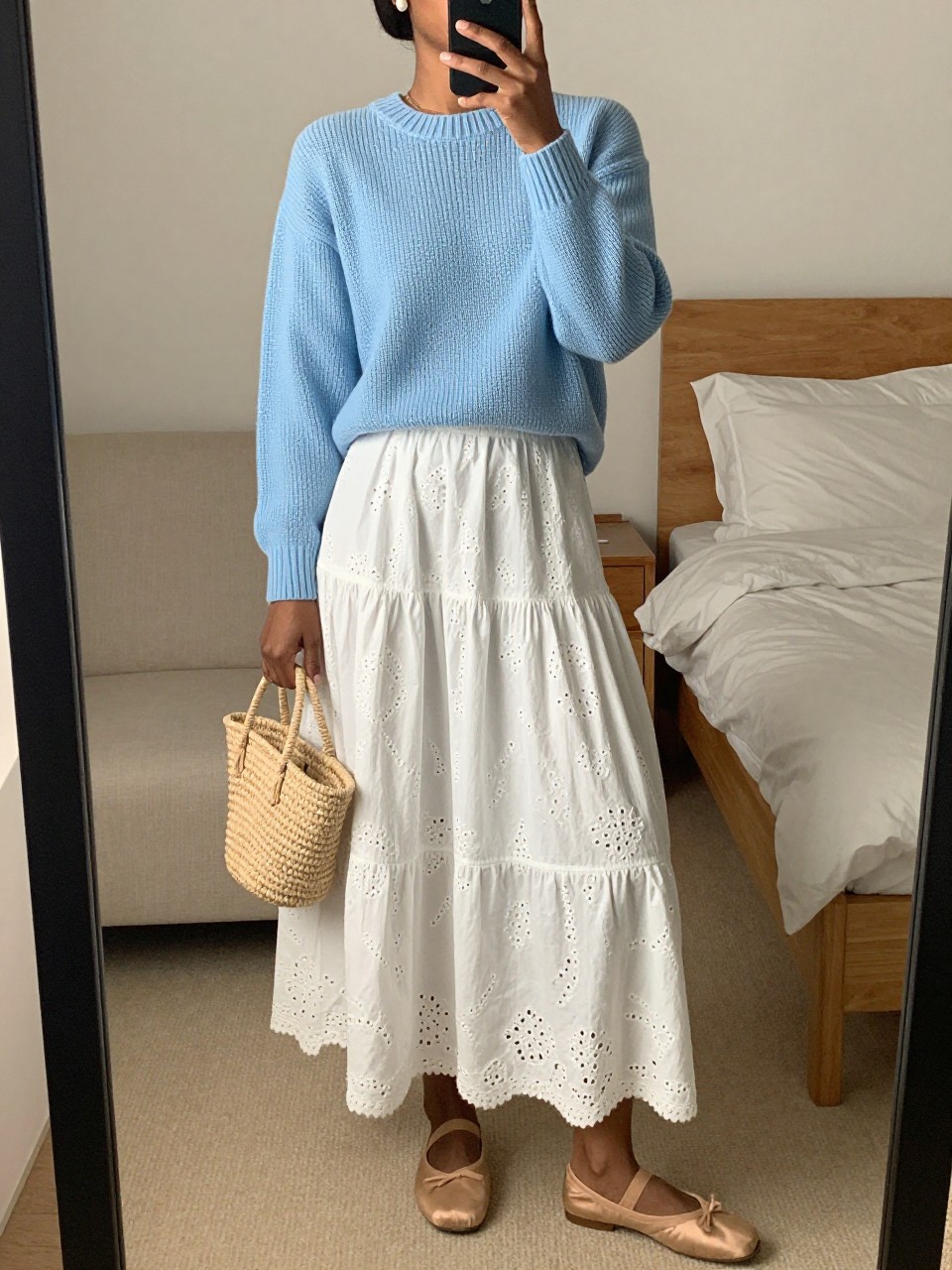 mirror selfie of a black woman wearing a baby blue fine-knit sweater tucked into a white eyelet maxi skirt with nude ballet flats and pearl stud earrings, holding a small straw bag, standing in a soft feminine pose, cropped at NECK so face doesn't show, in a feminine-themed bedroom, warm moody lighting, iPhone photo quality.