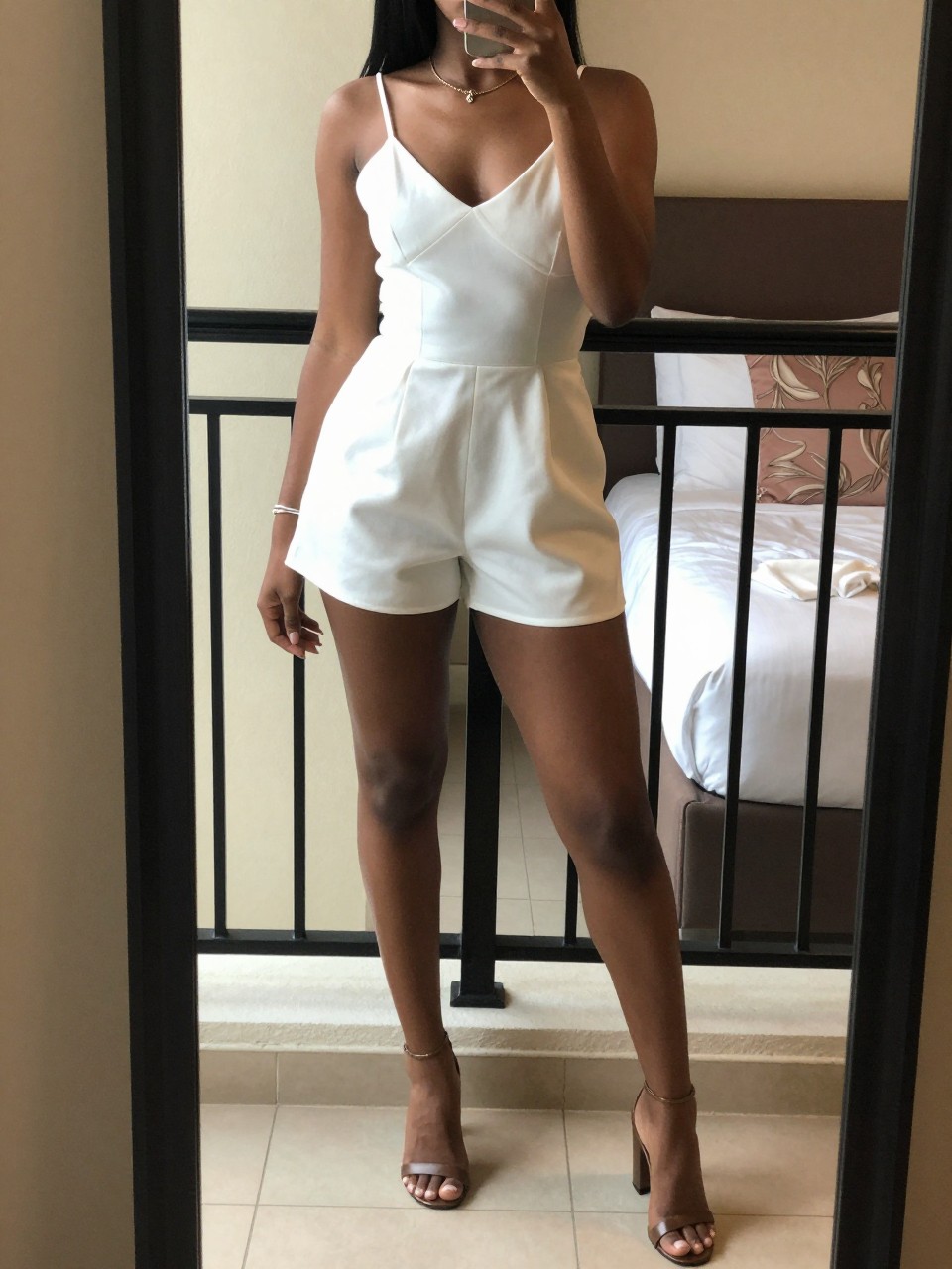 mirror selfie of a black woman in a white romper and block heels, standing on a hotel balcony, cropped at NECK so face doesn't show, in a feminine-themed bedroom, warm moody lighting, iPhone photo quality.