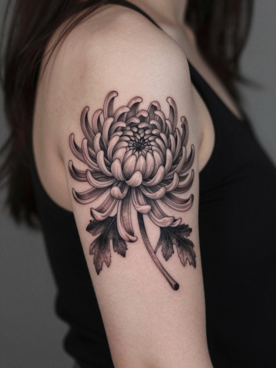 Image Prompt: "Design-focused close-up of a chrysanthemum flower sleeve tattoo on the arm, black and grey ink with many thin petals, soft shading, detailed floral layering, realistic skin texture, hair loosely falling near shoulder edge, feminine modern tattoo inspiration photo, minimal background, tattoo occupies most of the visual attention (no watermarks on images)"