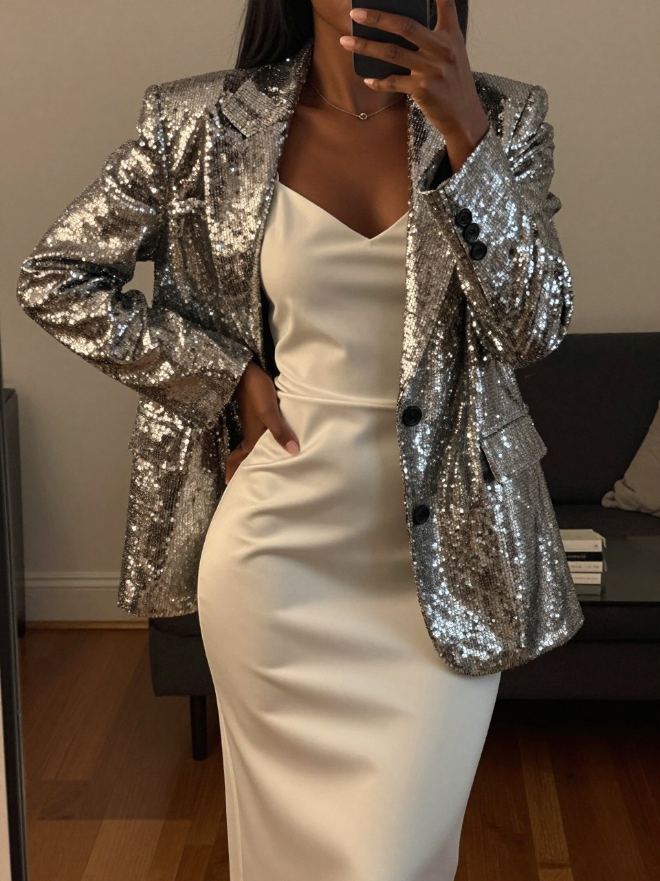 mirror selfie of a black woman in a sequined blazer and white slip skirt, hand resting on hip, cropped at NECK so face doesn't show, in a city apartment, warm moody lighting, iPhone photo quality.