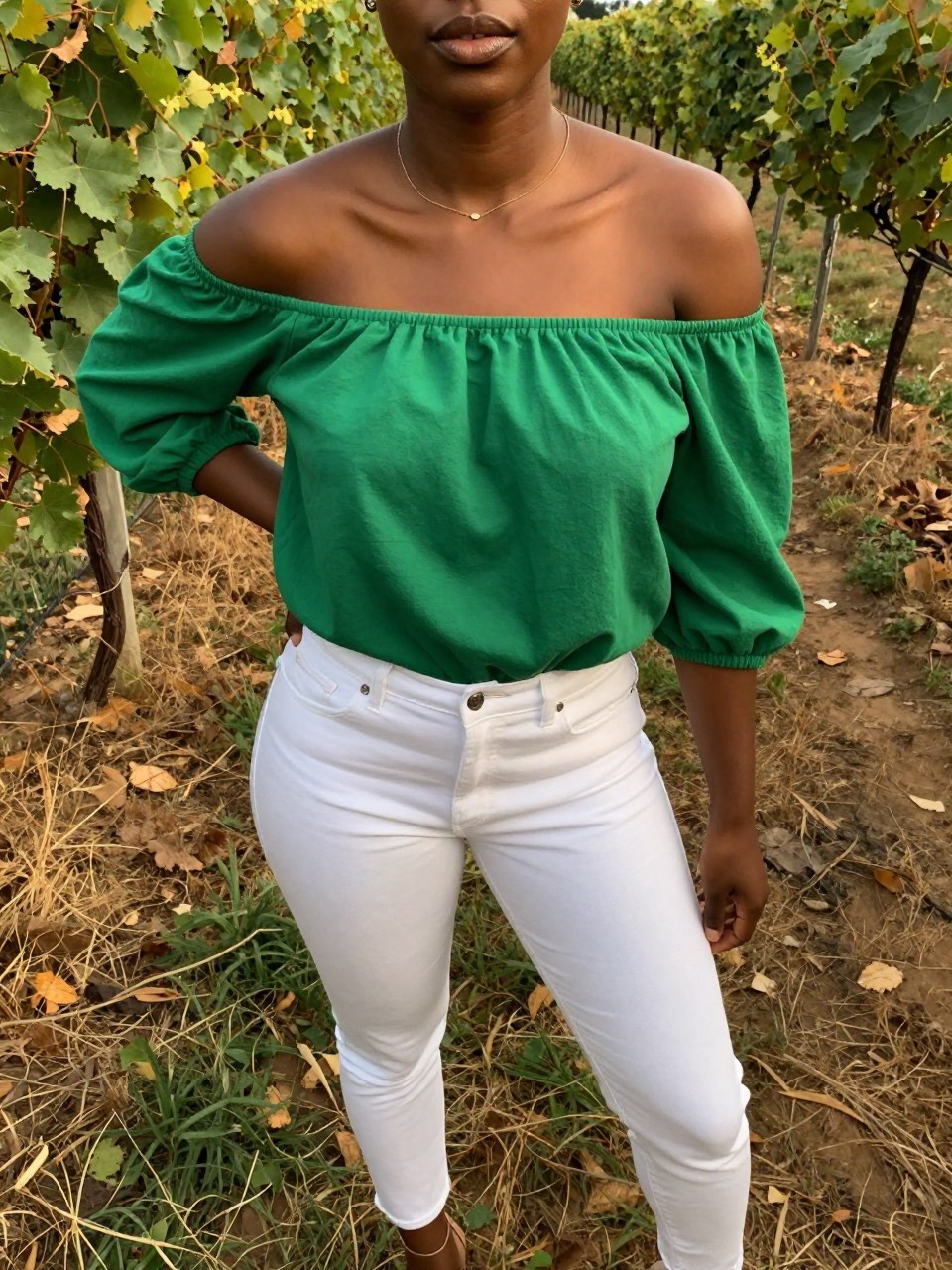 selfie of a black woman in a green off-shoulder top and white jeans with heels, standing on a vineyard path, cropped at NECK so face doesn't show, at a winery, warm moody lighting, iPhone photo quality.