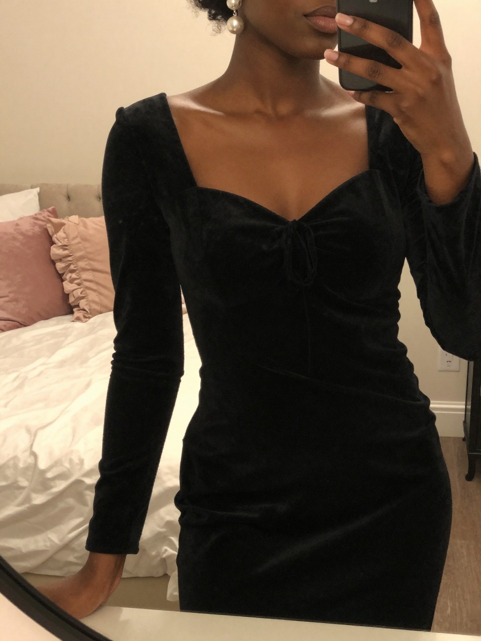 mirror selfie of a black woman in a black velvet dress, touching her pearl earring, cropped at NECK so face doesn't show, in a feminine-themed bedroom, warm moody lighting, iPhone photo quality.