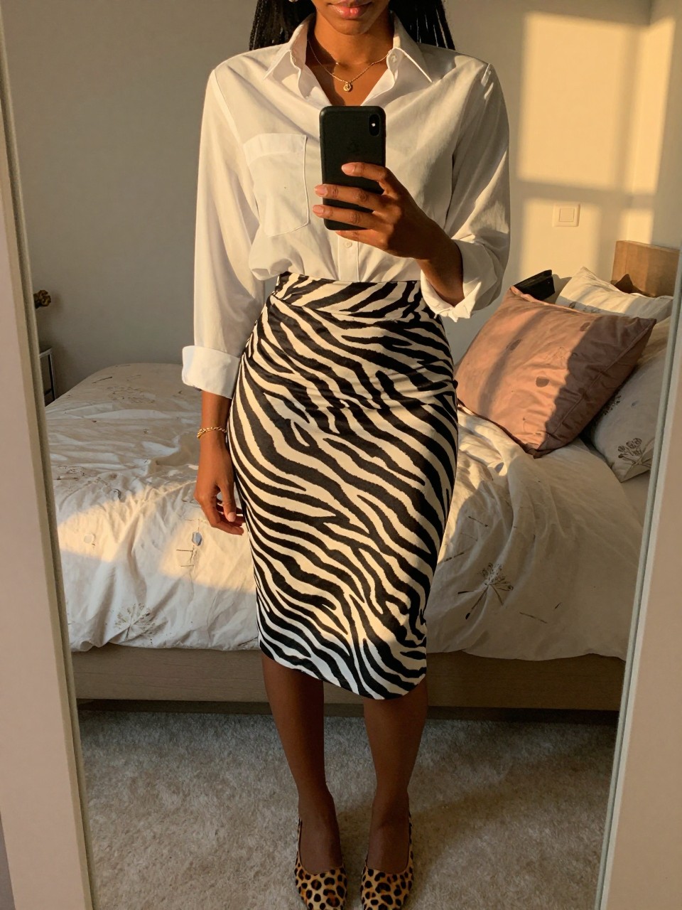 mirror selfie of a black woman in a white button-down shirt and a zebra print skirt with leopard print flats, holding her phone at waist level, cropped at NECK so face doesn't show, in a feminine-themed bedroom, evening golden hour, iPhone photo quality.