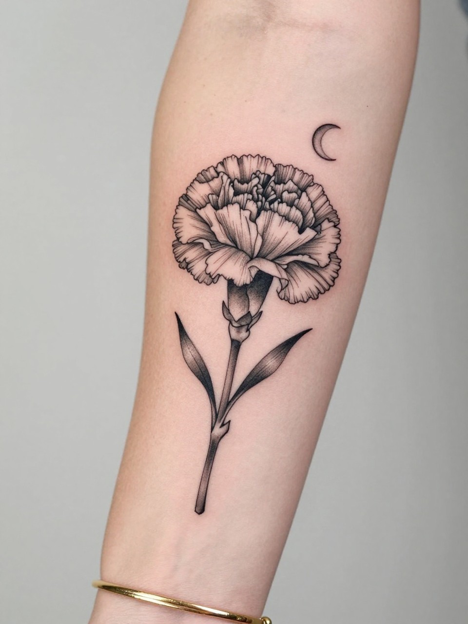 Image Prompt: "Design-focused close-up of a carnation tattoo with a tiny crescent moon on the inner arm, black ink fine line floral design, ruffled petals, soft shading, delicate celestial accent, realistic skin texture, gold bracelet lightly visible, feminine modern tattoo inspiration photo, clean soft background, tattoo is the hero (no watermarks on images)"