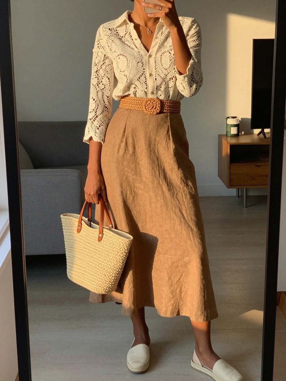 mirror selfie of a black woman wearing a cream lace blouse tucked into a tan brown linen midi skirt with a woven straw belt at her waist, holding a matching straw bag, wearing flat espadrilles, standing in a soft summer pose, cropped at NECK so face doesn't show, in a city apartment, evening golden hour, iPhone photo quality.