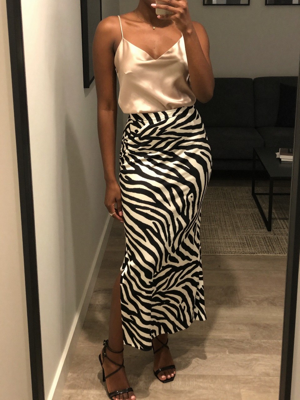 mirror selfie of a black woman in a champagne silk camisole and a zebra print maxi skirt with strappy heels, posing with one foot forward, cropped at NECK so face doesn't show, in a city apartment, warm moody lighting, iPhone photo quality.