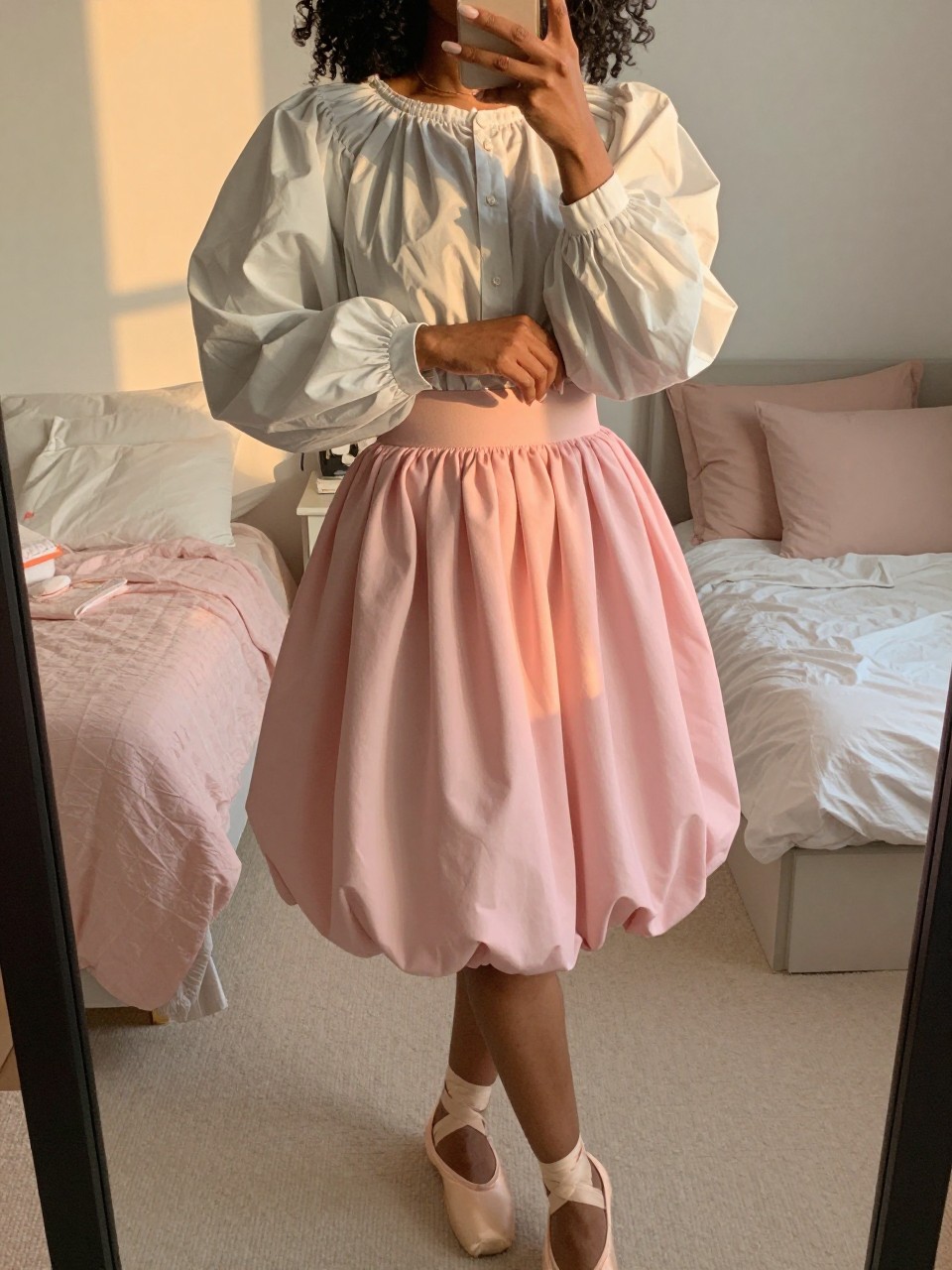 mirror selfie of a black woman in a puff-sleeve blouse and a pink balloon skirt with ballet flats, gently adjusting her sleeve, cropped at NECK so face doesn't show, in a feminine-themed bedroom, evening golden hour, iPhone photo quality.