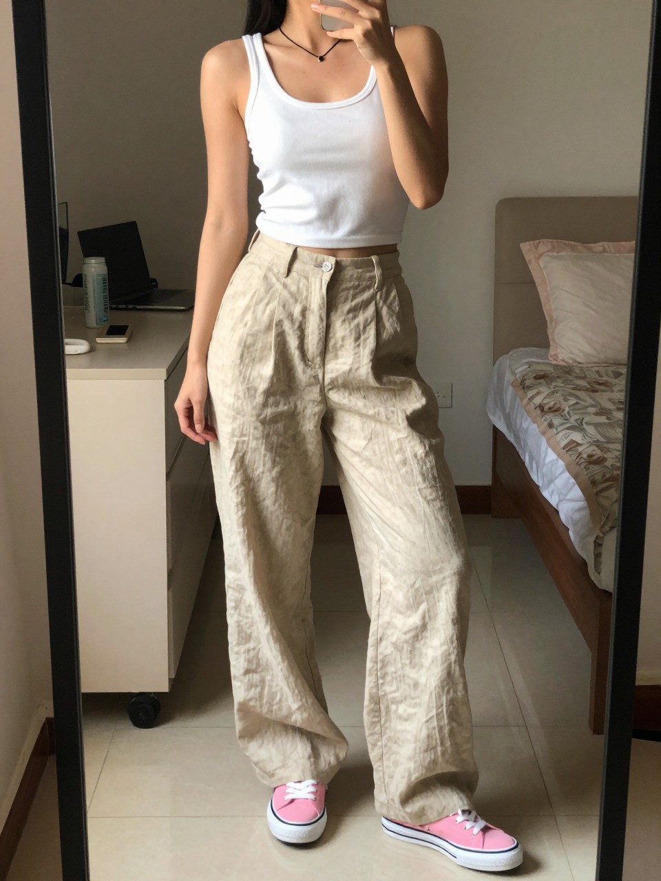iPhone mirror selfie of a woman in beige linen pants and a white tank with pink sneakers, standing with weight shifted, cropped at NECK so face doesn't show, in a feminine-themed bedroom, warm moody lighting, iPhone photo quality.
