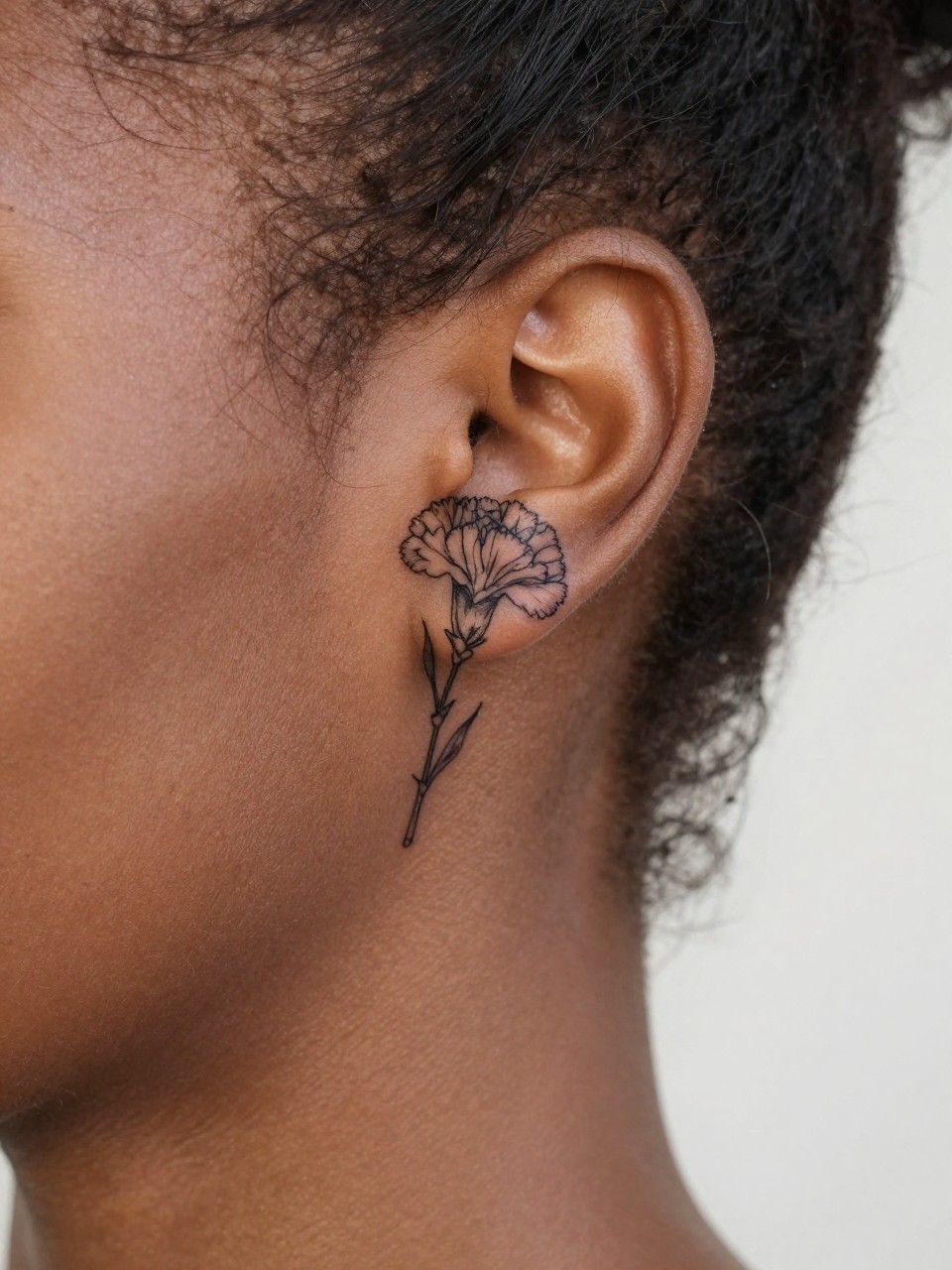 Image Prompt: "Macro shot of a tiny carnation flower tattoo behind the ear of a black woman, fine line black ink floral design with small ruffled petals and soft shading, realistic skin texture, a few loose strands of hair framing the placement, minimal feminine styling, tight crop, soft clean background, tattoo-centered inspiration image (no watermarks on images)"