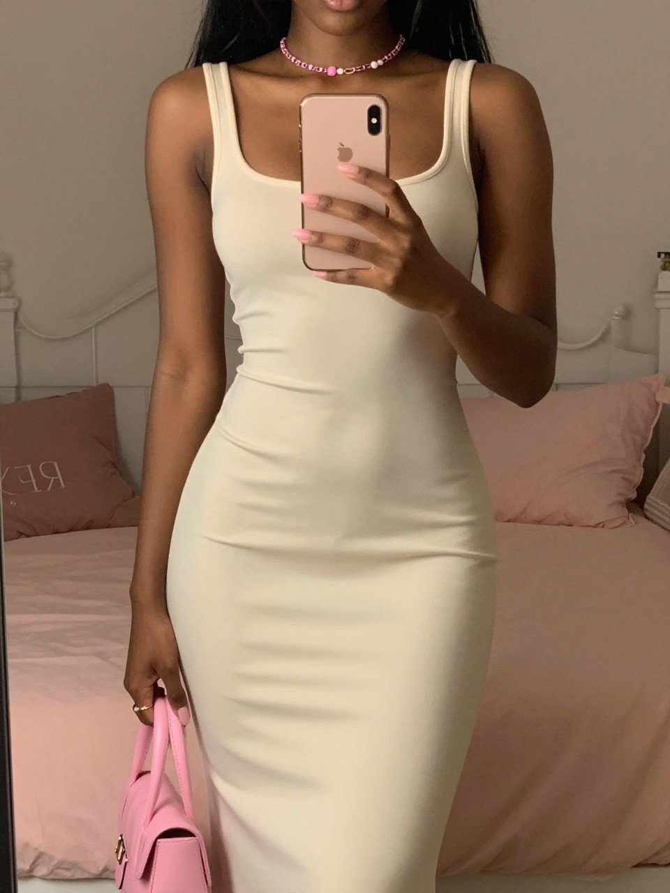 mirror selfie of a black woman in a cream dress with pink accessories, standing with phone at chest, cropped at NECK so face doesn't show, in a feminine-themed bedroom, warm moody lighting, iPhone photo quality.
