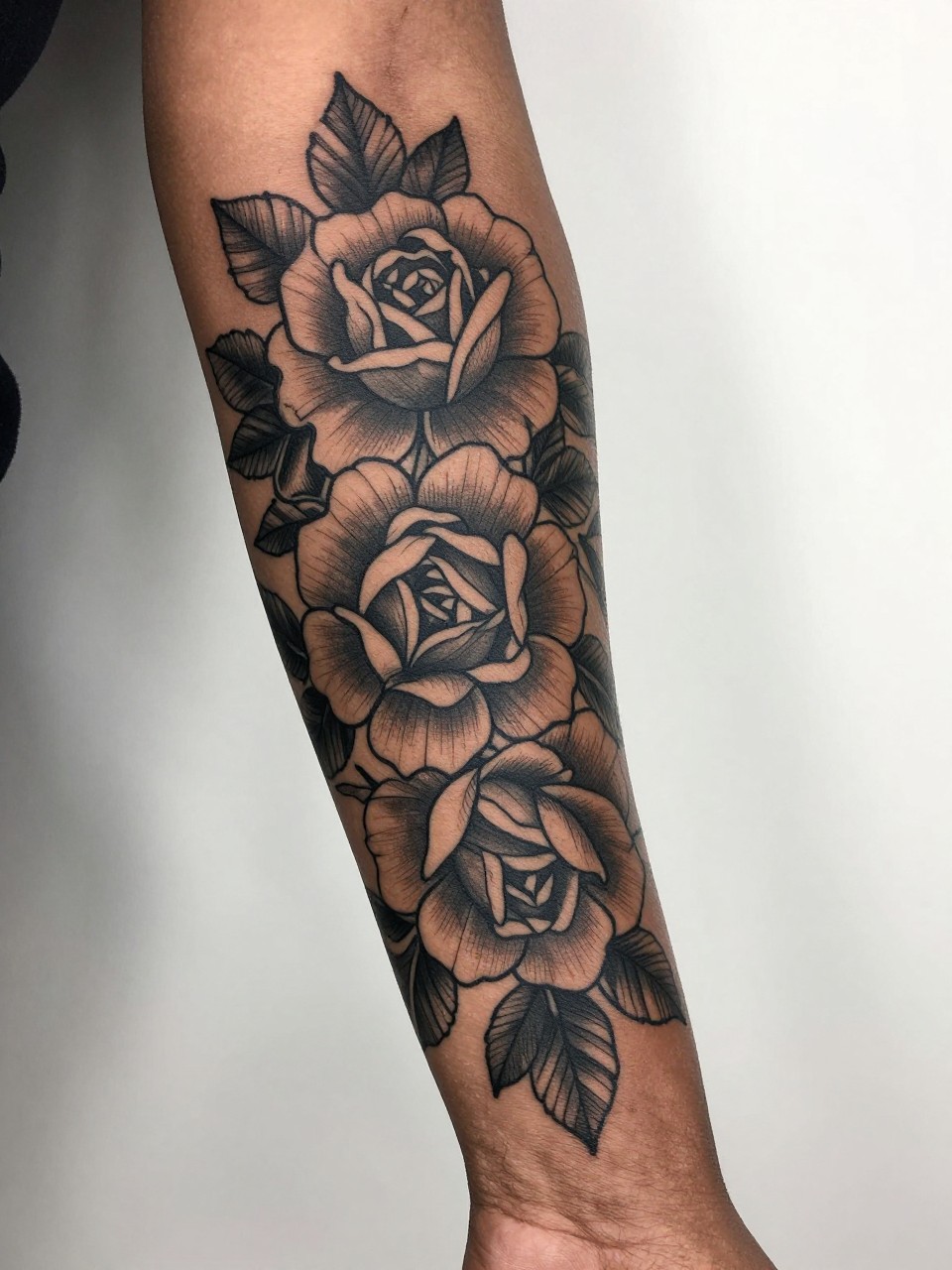 Image Prompt: "Extreme close-up of a blackwork flower sleeve tattoo on a black woman's full arm, bold floral design with dark roses and peonies, strong outline work, rich contrast, soft leaf fill, realistic skin texture, design-first composition, minimal feminine styling, clean background, modern tattoo inspiration photo, tattoo fills most of the image (no watermarks on images)"