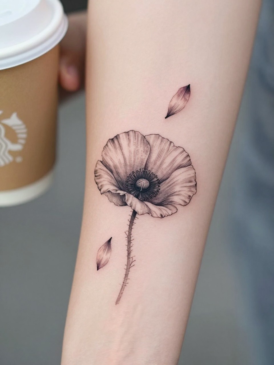 Image Prompt: "Extreme close-up of a fine line poppy tattoo with a few falling petals on the forearm, black ink floral design, delicate petal movement, soft shading, realistic skin texture, coffee cup softly blurred nearby, modern feminine tattoo inspiration image, minimal background, tattoo-centered composition (no watermarks on images)"