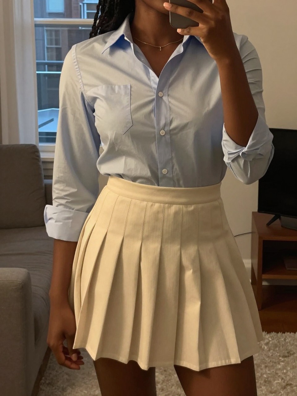 mirror selfie of a black woman in a button-down and pleated skirt, tucking in her shirt, cropped at NECK so face doesn't show, in a city apartment, warm moody lighting, iPhone photo quality.