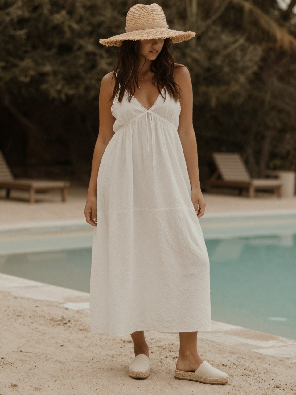 photo of a woman in a white maxi dress and espadrilles with a straw hat, standing on a beach or at a pool, cropped at NECK so face doesn't show, warm moody lighting, iPhone photo quality.