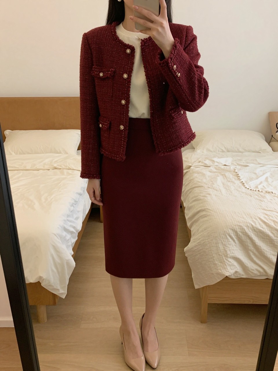 mirror selfie of a woman wearing a burgundy tweed jacket over a cream shell tucked into a deep burgundy pencil skirt with pearl earrings and nude pumps, one hand resting on her jacket, cropped at NECK so face doesn't show, in a feminine-themed bedroom, warm moody lighting, iPhone photo quality.