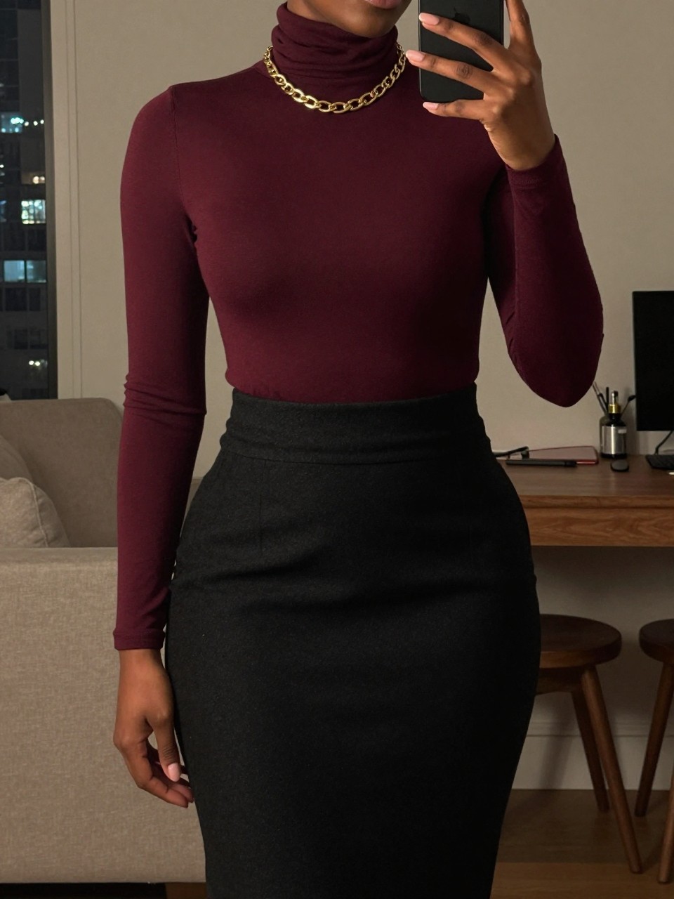 iPhone mirror selfie of a black woman wearing a burgundy turtleneck tucked into a black wool pencil skirt with a chunky gold chain necklace, standing straight with her phone held at her side, cropped at NECK so face doesn't show, in a city apartment, warm moody lighting, iPhone photo quality.