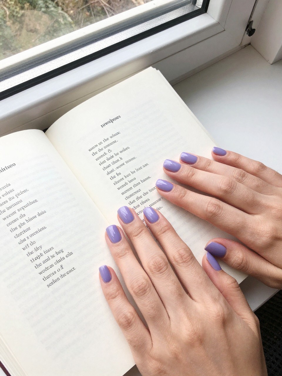 Image Prompt: Top-down view of hands with neat, short nails resting on a page of a poetry book. The nails are a cool-toned, matte wisteria purple. The setting is a quiet, sunlit reading nook by a window, creating a peaceful mood.