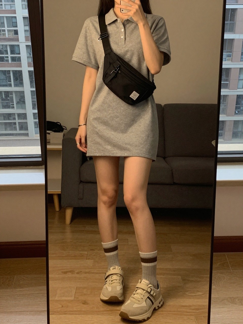 iPhone mirror selfie of a woman in a polo dress and grip socks, holding a fanny pack, cropped at NECK so face doesn't show, in a city apartment, warm moody lighting, iPhone photo quality.