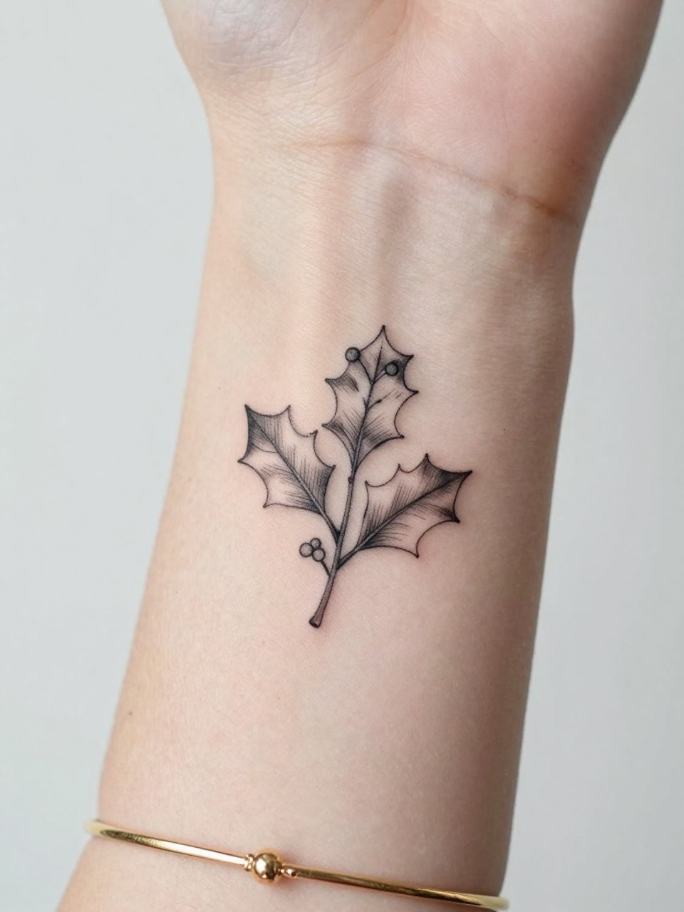 Image Prompt: "Macro shot of a tiny holly sprig tattoo on the inner wrist, black ink fine line leaves with tiny berry details and soft shading, minimalist floral style, realistic skin texture, delicate gold bracelet, tight crop, feminine tattoo inspiration image, clean minimal background, tattoo-centered composition (no watermarks on images)"