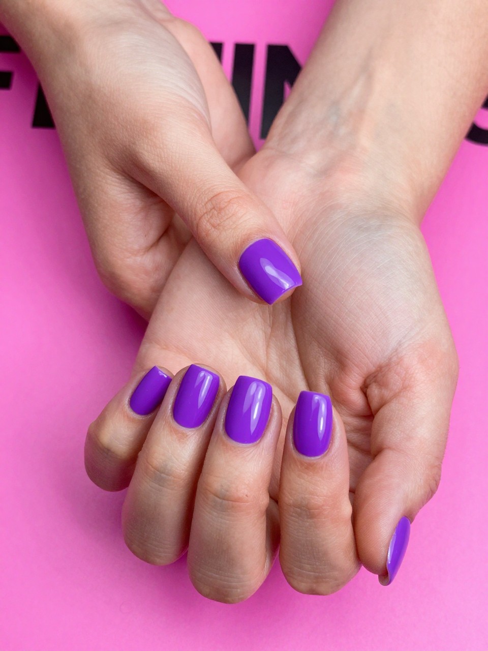 Image Prompt: Top-down view of hands with short, squared nails on a neon pink magazine. The nails are a bold, matte violet. The lunula at the base is filled with a high-gloss top coat, creating a shiny, defined crescent. The look is playful and modern.