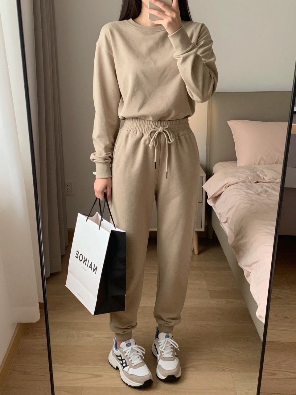 iPhone mirror selfie of a woman in a matching jogger set and sneakers, holding a party bag, cropped at NECK so face doesn't show, in a feminine-themed bedroom, warm moody lighting, iPhone photo quality.