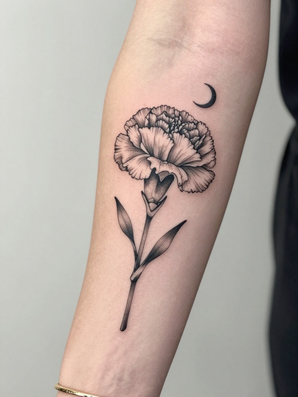 Image Prompt: "Design-focused close-up of a carnation tattoo with a tiny crescent moon on the inner arm, black ink fine line floral design, layered ruffled petals, soft shading, delicate celestial accent, realistic skin texture, gold bracelet lightly visible, feminine modern tattoo inspiration photo, clean soft background, tattoo is the hero (no watermarks on images)"