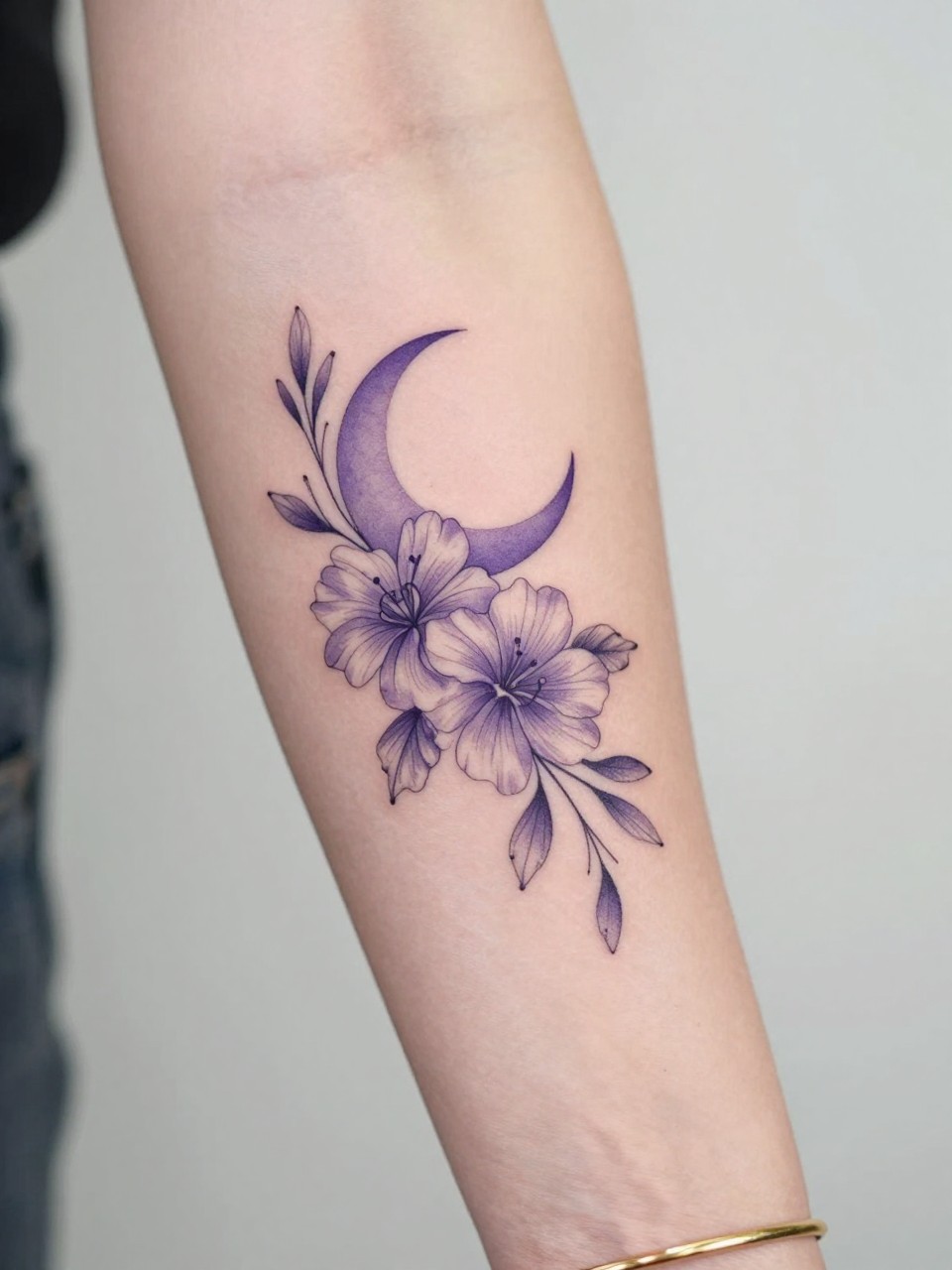 Image Prompt: "Design-focused close-up of a violet tattoo with a tiny crescent moon on the inner arm, black ink fine line floral design, rounded petals, soft shading, delicate celestial accent, realistic skin texture, gold bracelet lightly visible, feminine modern tattoo inspiration photo, clean soft background, tattoo is the hero (no watermarks on images)"