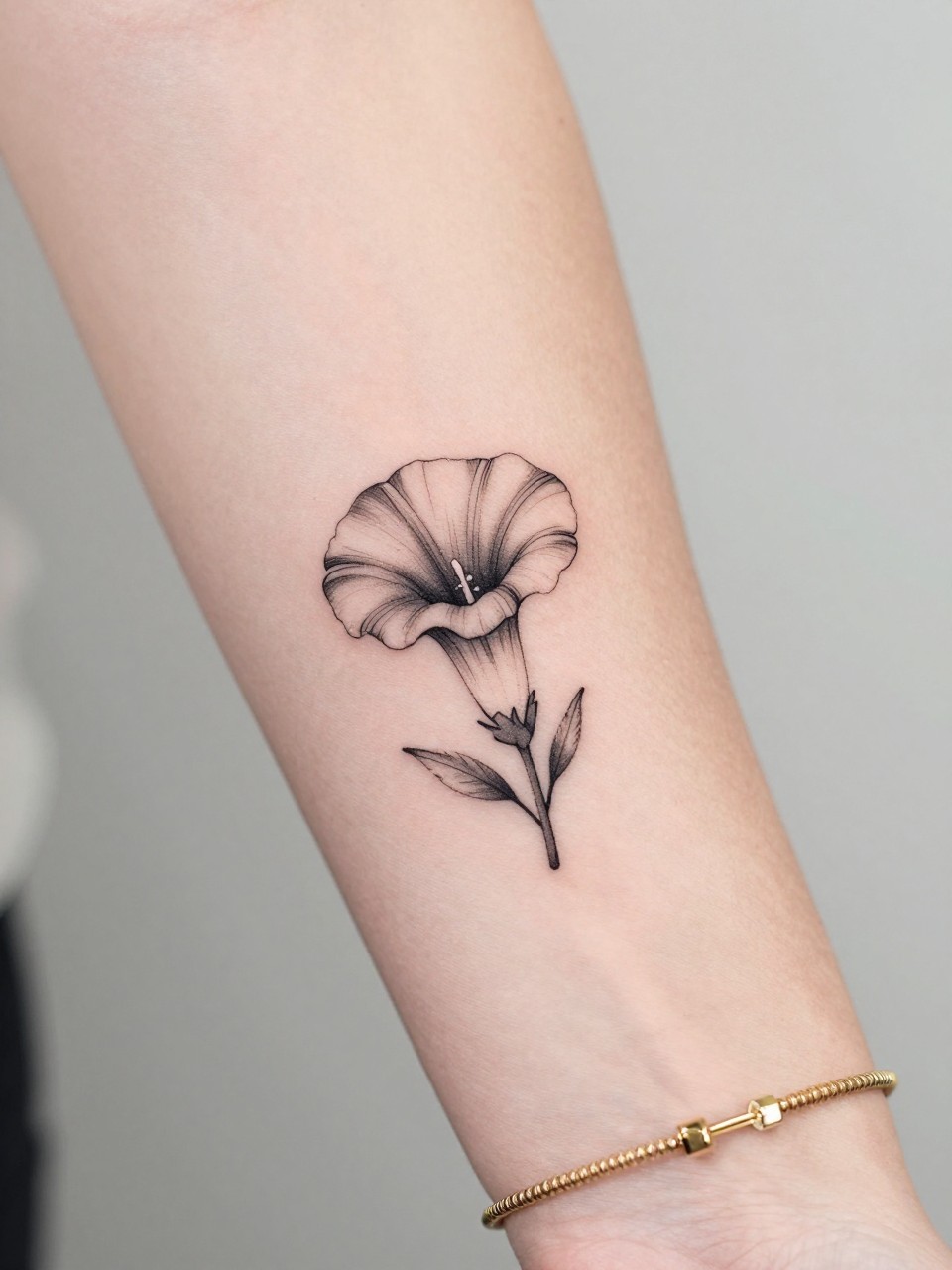 Image Prompt: "Macro shot of a tiny morning glory flower tattoo on the inner wrist, black ink fine line floral design with soft trumpet-shaped petals and light shading, minimalist style, realistic skin texture, delicate gold bracelet, tight crop, feminine tattoo inspiration image, clean minimal background, tattoo-centered composition (no watermarks on images)"