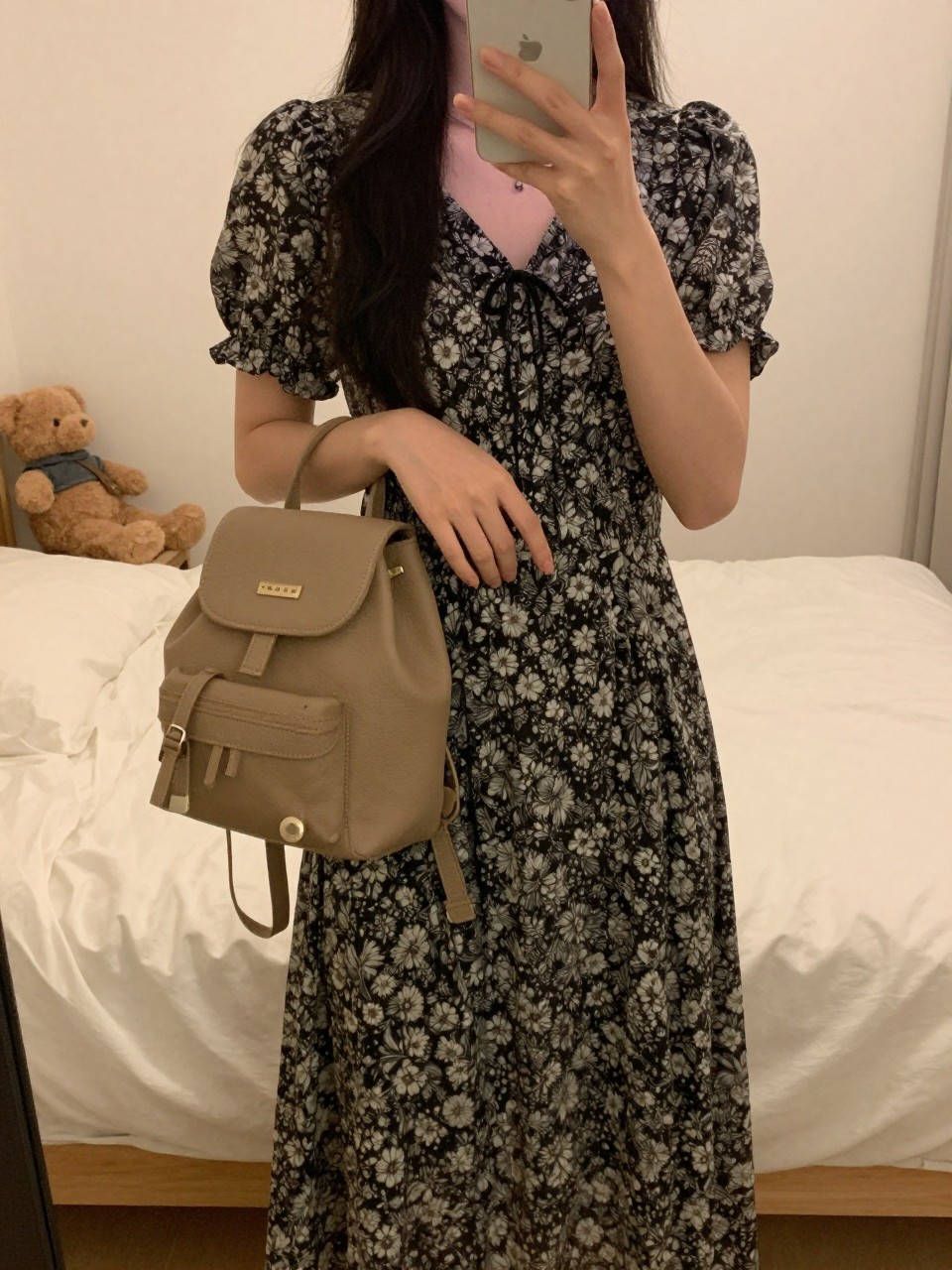 iPhone mirror selfie of a woman in a patterned midi dress, holding a mini backpack, cropped at NECK so face doesn't show, in a feminine-themed bedroom, warm moody lighting, iPhone photo quality.