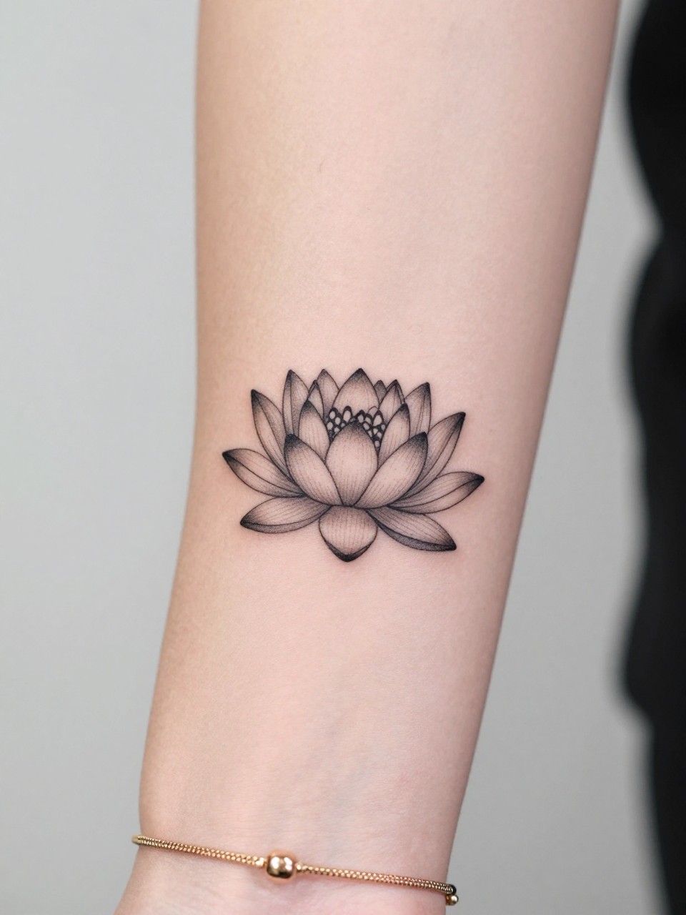 Image Prompt: "Macro shot of a small water lily tattoo on the inner wrist, black ink fine line design with soft shading, rounded layered petals, minimalist floral style, realistic skin texture, delicate gold bracelet, tight crop, feminine tattoo inspiration image, clean minimal background, tattoo-centered composition (no watermarks on images)"
