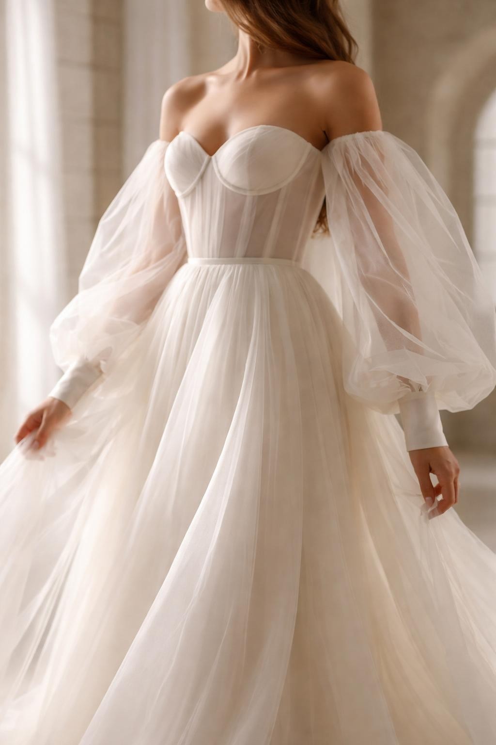 Image Prompt: A fashion-forward bridal editorial photo of a wedding dress with long puff sleeves made from sheer organza, styled in an elegant chapel or editorial bridal studio. Show the bride cropped from the neck down or from a back-side angle with the face fully hidden. The gown has airy long puff sleeves, a structured bodice, soft flowing skirt, and romantic movement. Use clean natural light, realistic organza texture, luxury bridal editorial styling, no visible face, no text, no watermark. (no watermarks on images)