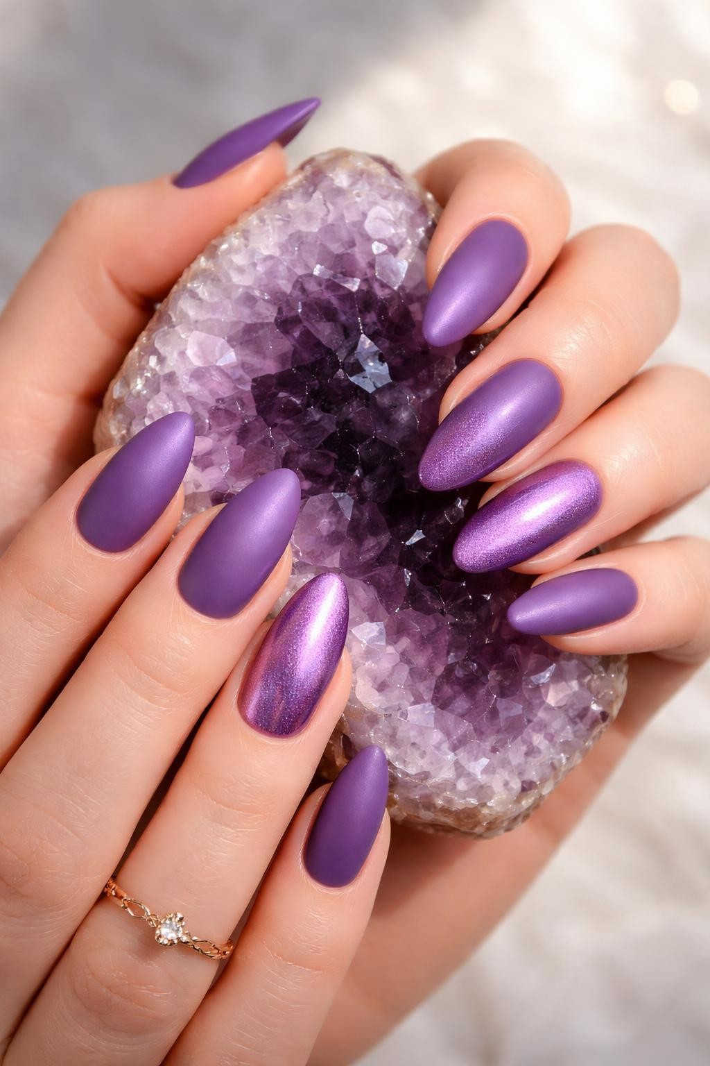 Image Prompt: Bird's-eye view of hands with almond nails gently holding a crystal geode. Most nails are a rich matte violet. The ring fingers are painted in a shimmery, metallic violet polish. Light reflects off the metallic nails and crystal.