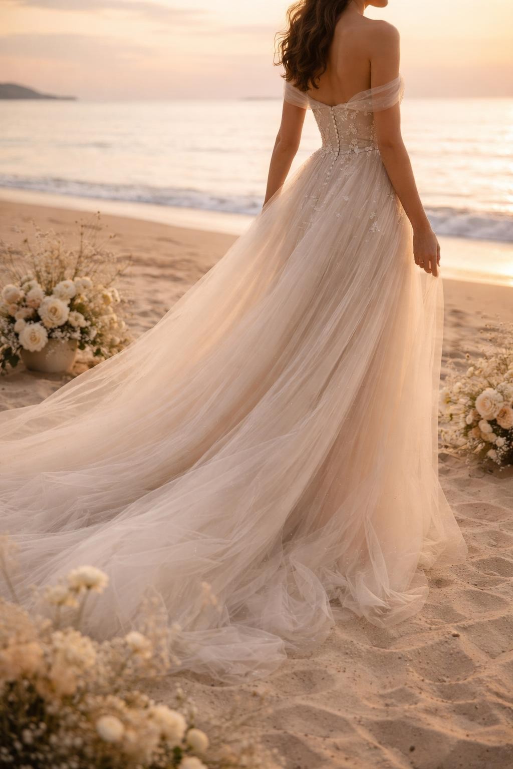 Image Prompt: A romantic bridal editorial image of a soft tulle beach wedding gown at sunset with pale sand, calm water, and simple floral styling. Show the bride from the neck down or from a back-side angle with the face not visible. The gown has a light fitted bodice, soft layered tulle skirt, subtle shimmer or delicate appliqué, and gentle movement in the breeze. Use warm natural light, realistic tulle texture, airy editorial composition, luxury wedding magazine quality, no visible face, no text, no watermark. (no watermarks on images)