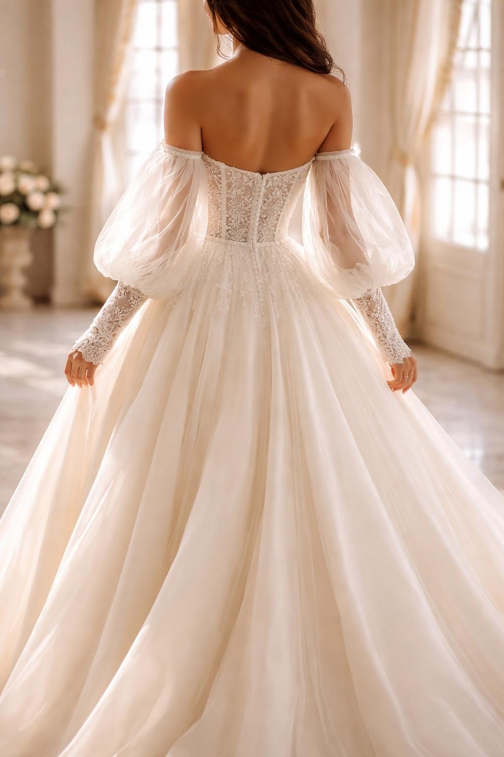 Image Prompt: A luxury bridal editorial image of a corset wedding dress styled with detachable sleeves in an elegant chapel, bridal studio, or estate venue. Show the bride from the neck down only, or from behind with the face fully hidden. The gown has a structured corset bodice, defined waist, flowing skirt, and detachable off-shoulder sleeves or sheer long sleeves. Use soft natural light, realistic fabric texture, polished bridal editorial styling, no visible face, no text, no watermark. (no watermarks on images)