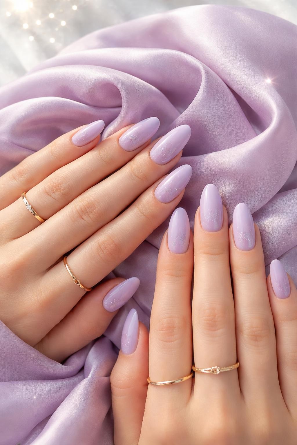 Image Prompt: Bird's-eye view of hands with medium almond nails resting on a lilac silk scarf. The nails are a soft matte lilac. A delicate fade of silver glitter blends from the cuticle line into the base color. The setting is bright and airy, catching the glitter's sparkle.