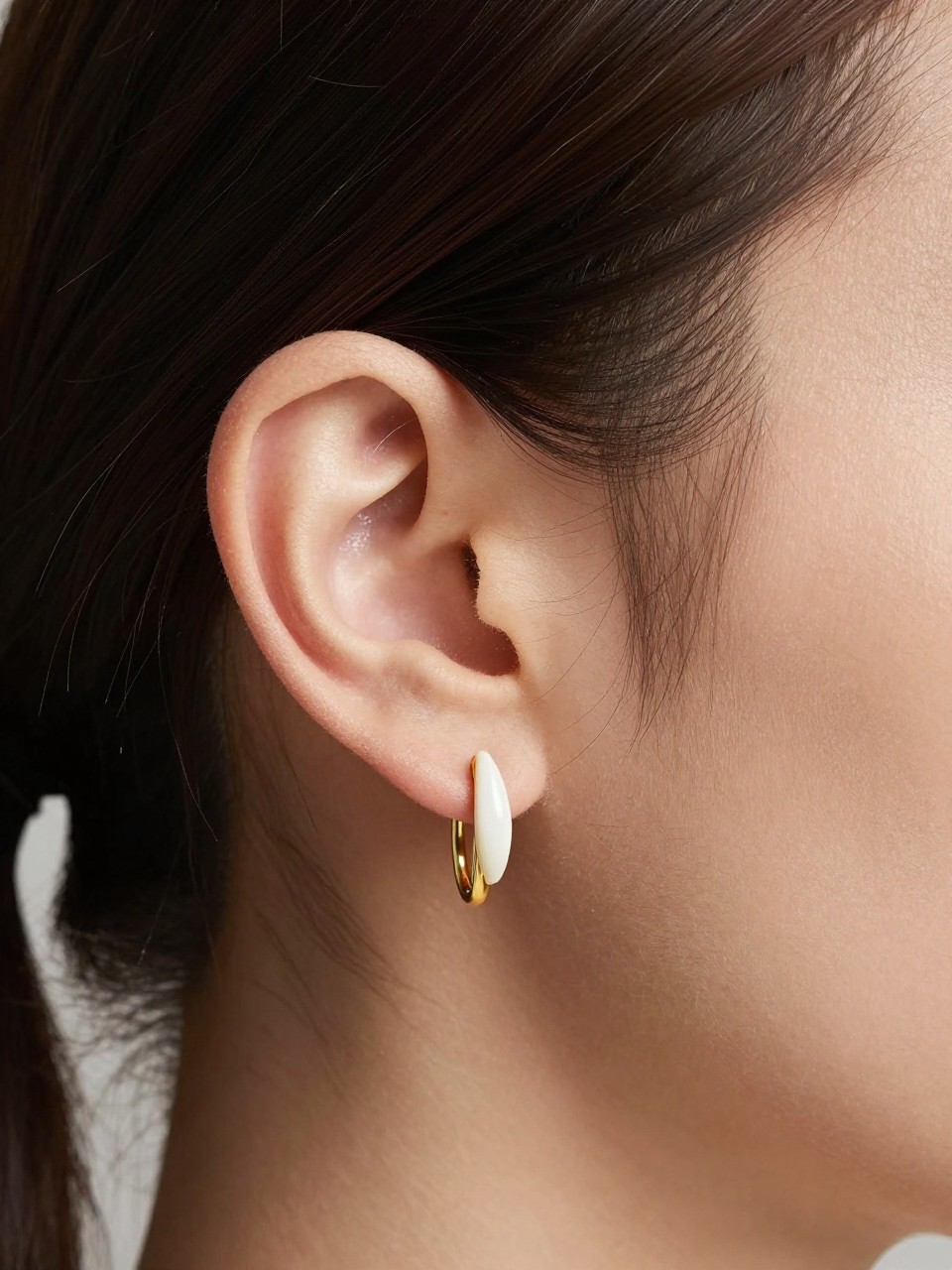 Extreme close-up of a woman’s ear with fair skin tone, hair pinned back cleanly, one slim gold tragus hoop and one polished conch ring creating a minimal armor-like look, soft directional lighting, realistic skin texture, sharp high-end beauty editorial focus on the ear.