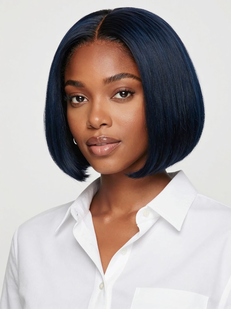 Image Prompt: A pretty black woman with a chin-length black blue bob, smooth rounded bob shape with a soft bend at the ends, dark black-blue hair color with glossy navy shine, medium skin tone, fresh natural makeup, glossy nude lips, small silver earrings, white button-up shirt, bright clean studio background, soft flattering lighting, realistic beauty editorial photography, detailed bob shape and blue-black shine, no text, (no watermarks on images)