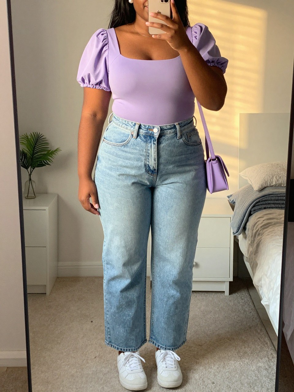 Mirror selfie of a black plus size woman wearing light-wash high-waisted straight-leg jeans, a fitted lavender top with short puff sleeves and a square neckline, white leather sneakers, a small lavender crossbody bag, and pearl stud earrings, clearly showing the exact clothing items, light denim, lavender fabric, sleeve shape, white footwear, and accessories listed, holding a phone in front of a mirror, cropped at the neck so her face does not appear, relaxed friendly selfie stance, in a feminine-themed bedroom with evening golden-hour lighting, a small plant on a dresser and a folded blanket on a chair, realistic coffee-date outfit, latest iPhone photo quality.