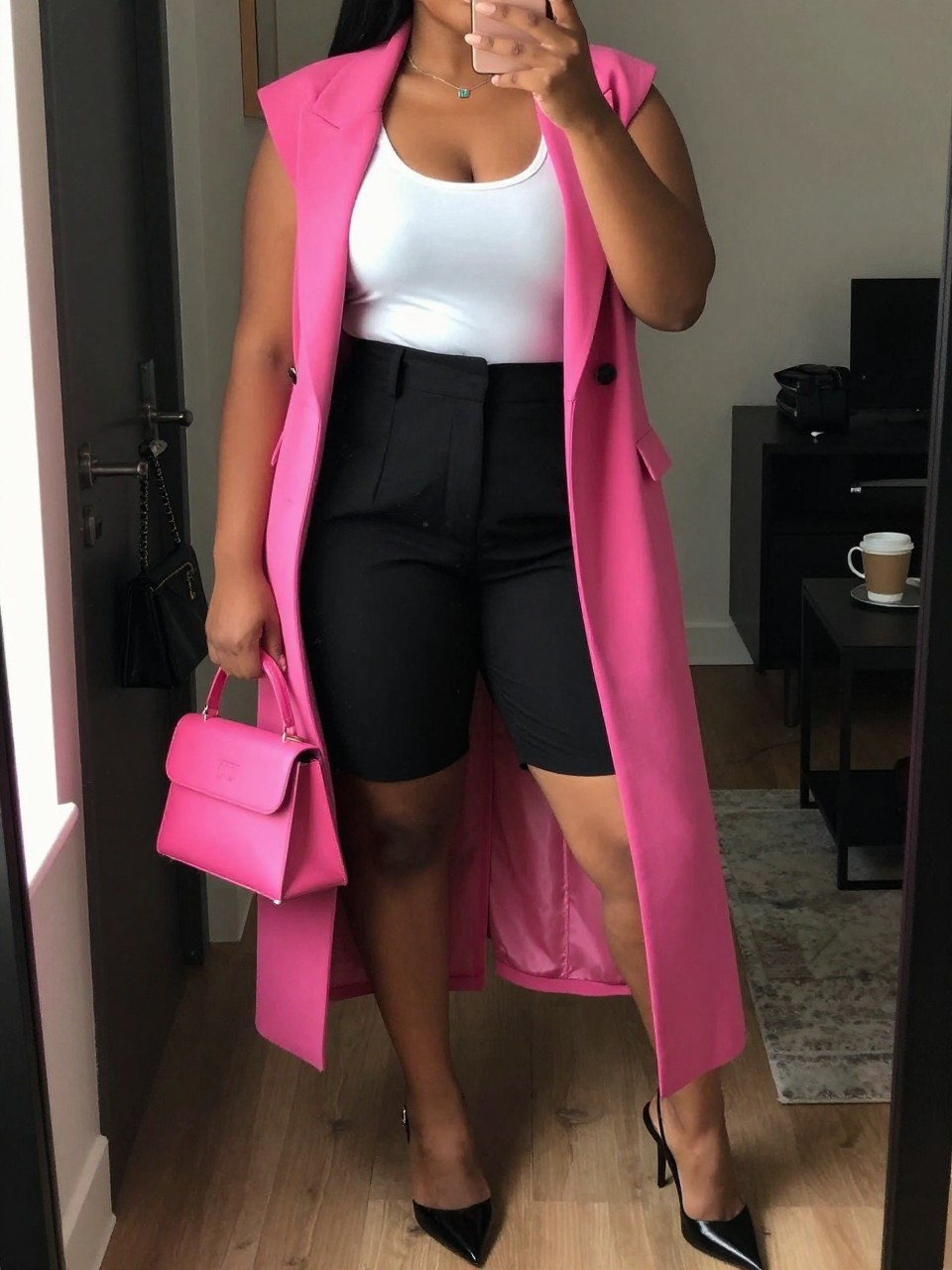 Mirror selfie of a black plus size woman wearing high-waisted black tailored shorts with a long relaxed cut, a fitted white scoop-neck tank top, a hot pink sleeveless longline blazer worn open, black pointed slingback heels, and a small hot pink structured handbag, clearly showing the exact clothing items, black shorts, white tank, pink blazer, colors, footwear, and accessories listed, holding a phone in front of a mirror, cropped at the neck so the face does not show, relaxed bold selfie stance, in a stylish city apartment with warm moody lighting, a handbag hanging on a door handle and a coffee mug on a side table, realistic polished summer outfit, latest iPhone photo quality.